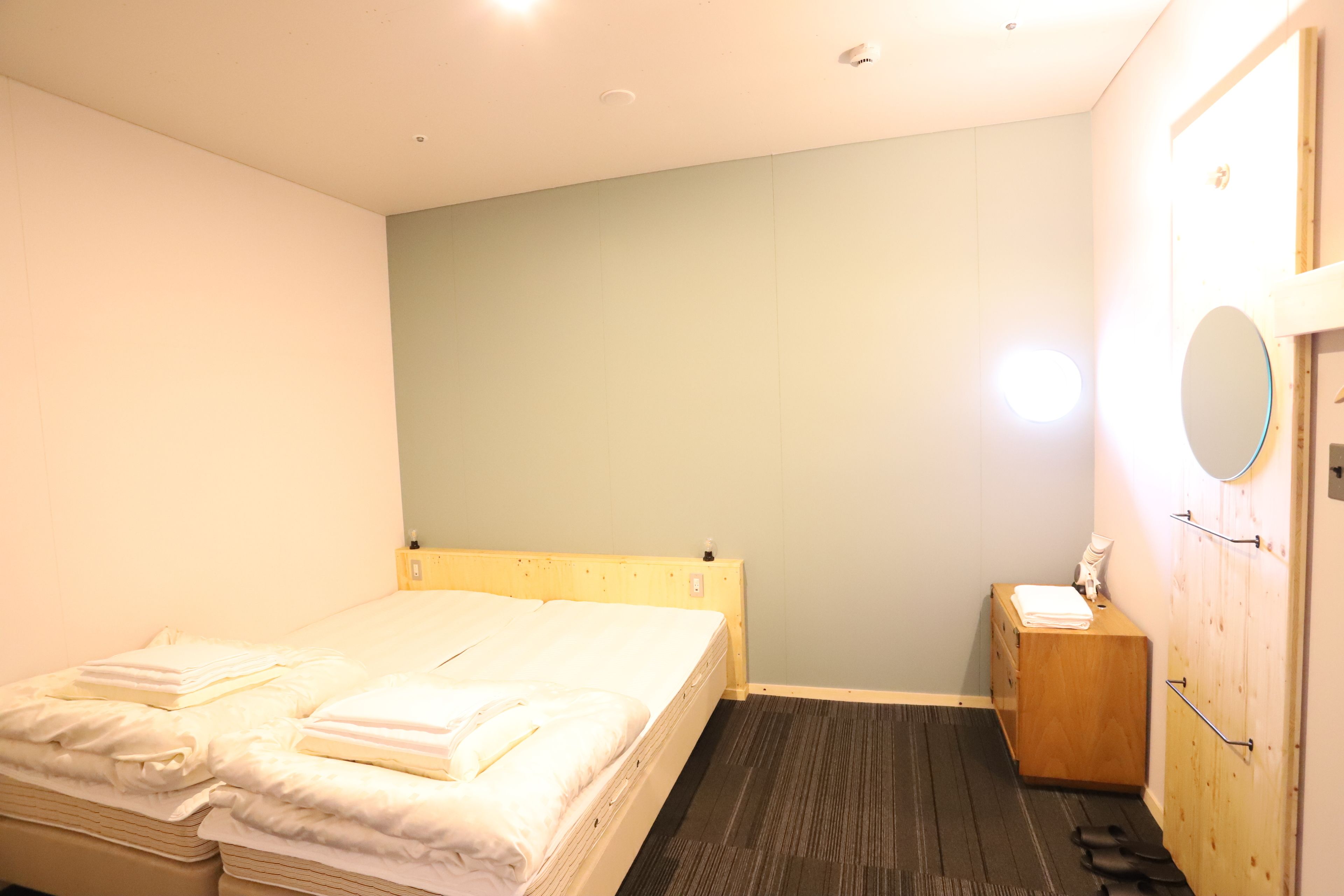 A bedroom with a bed, a wooden dresser, a mirror, and a small bedside table.