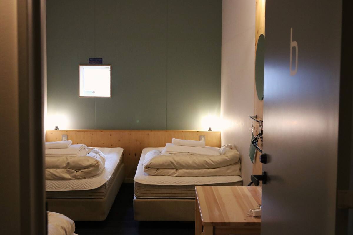 A room with two beds, a wooden table, and a wall-mounted light.