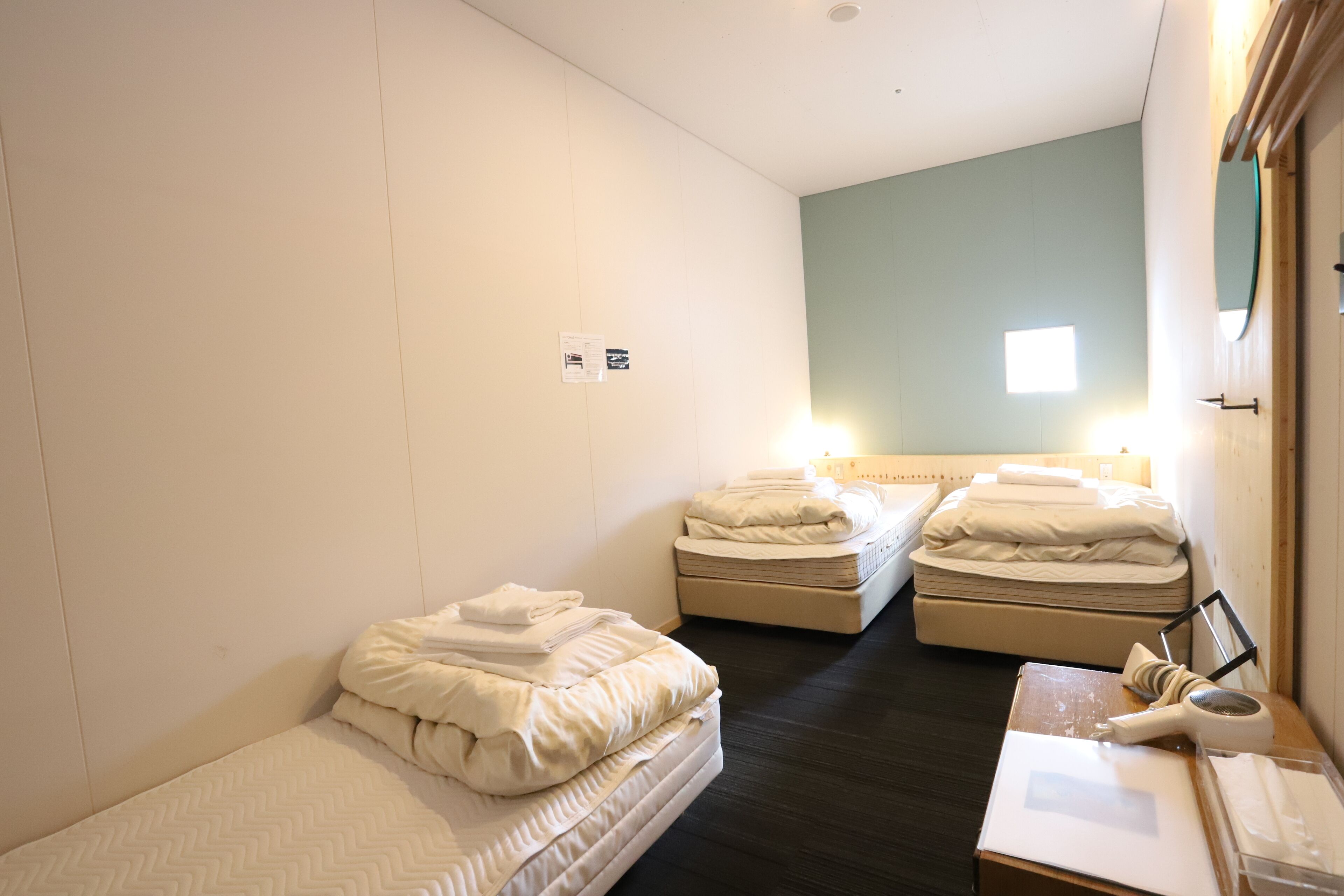 A hotel room with two single beds, a small table with a lamp, and a window with natural light.