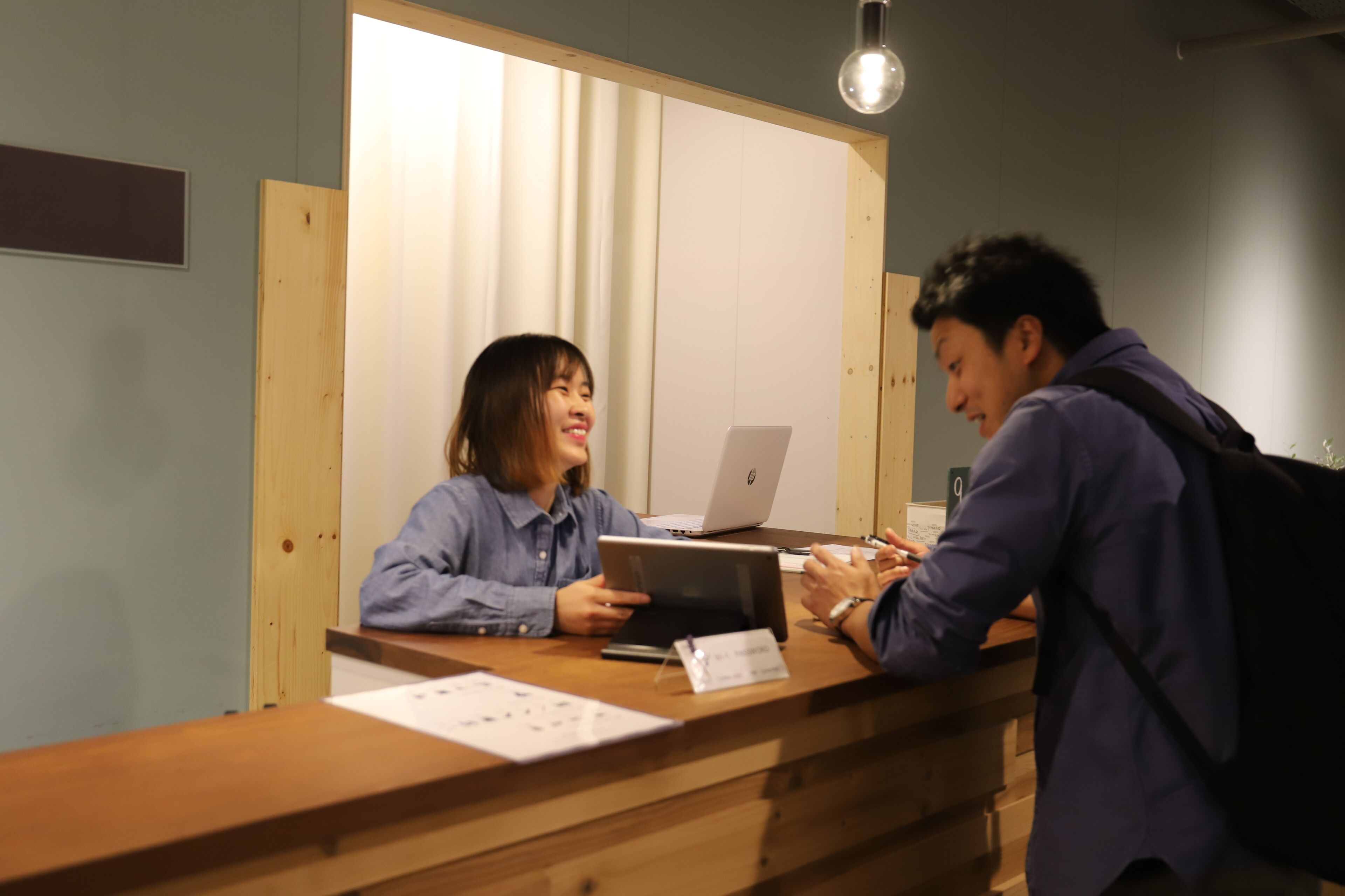 A reception desk with a wooden counter, a laptop, and papers on the desk.