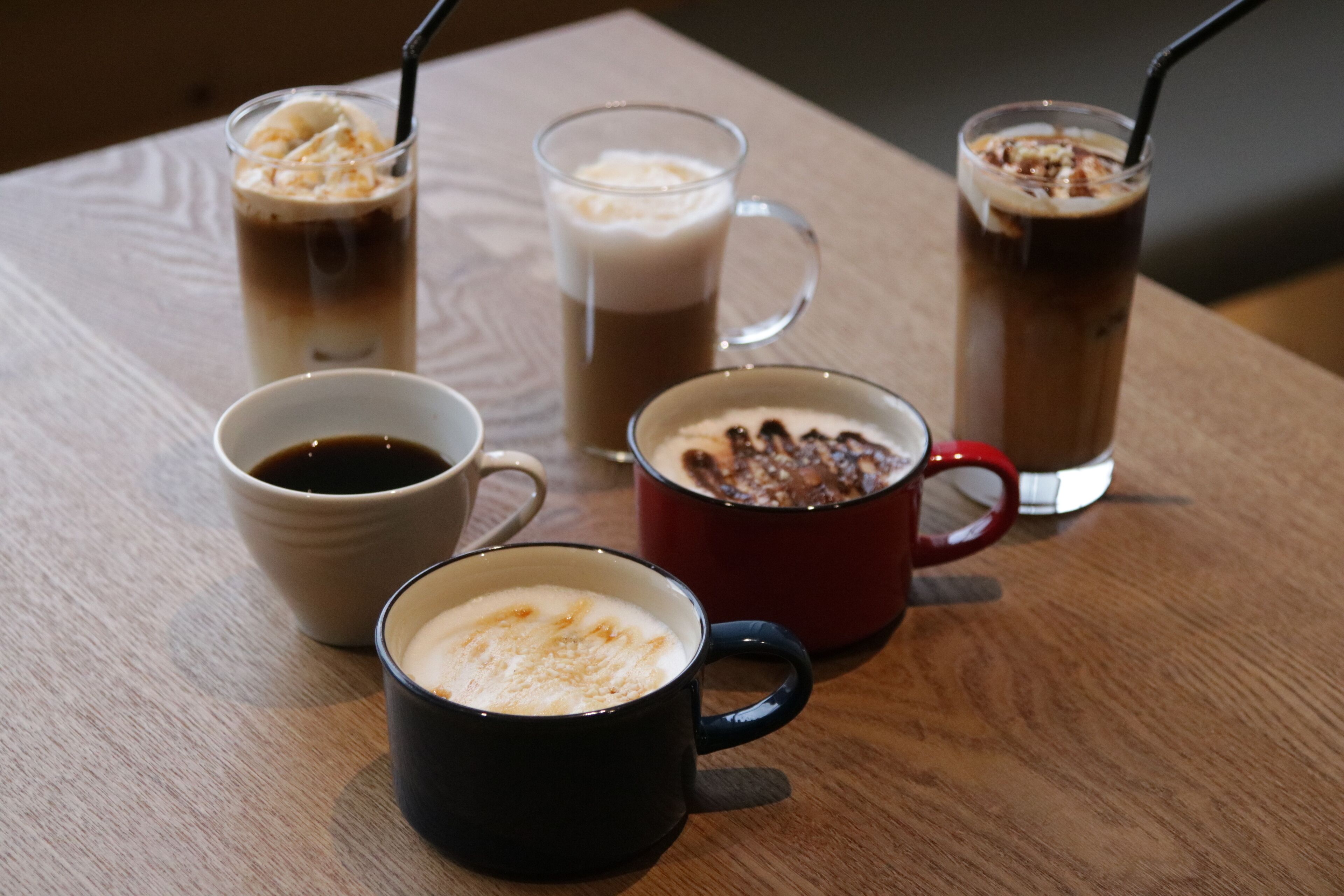 A wooden table with four cups of beverages, including coffee and iced drinks, with straws.