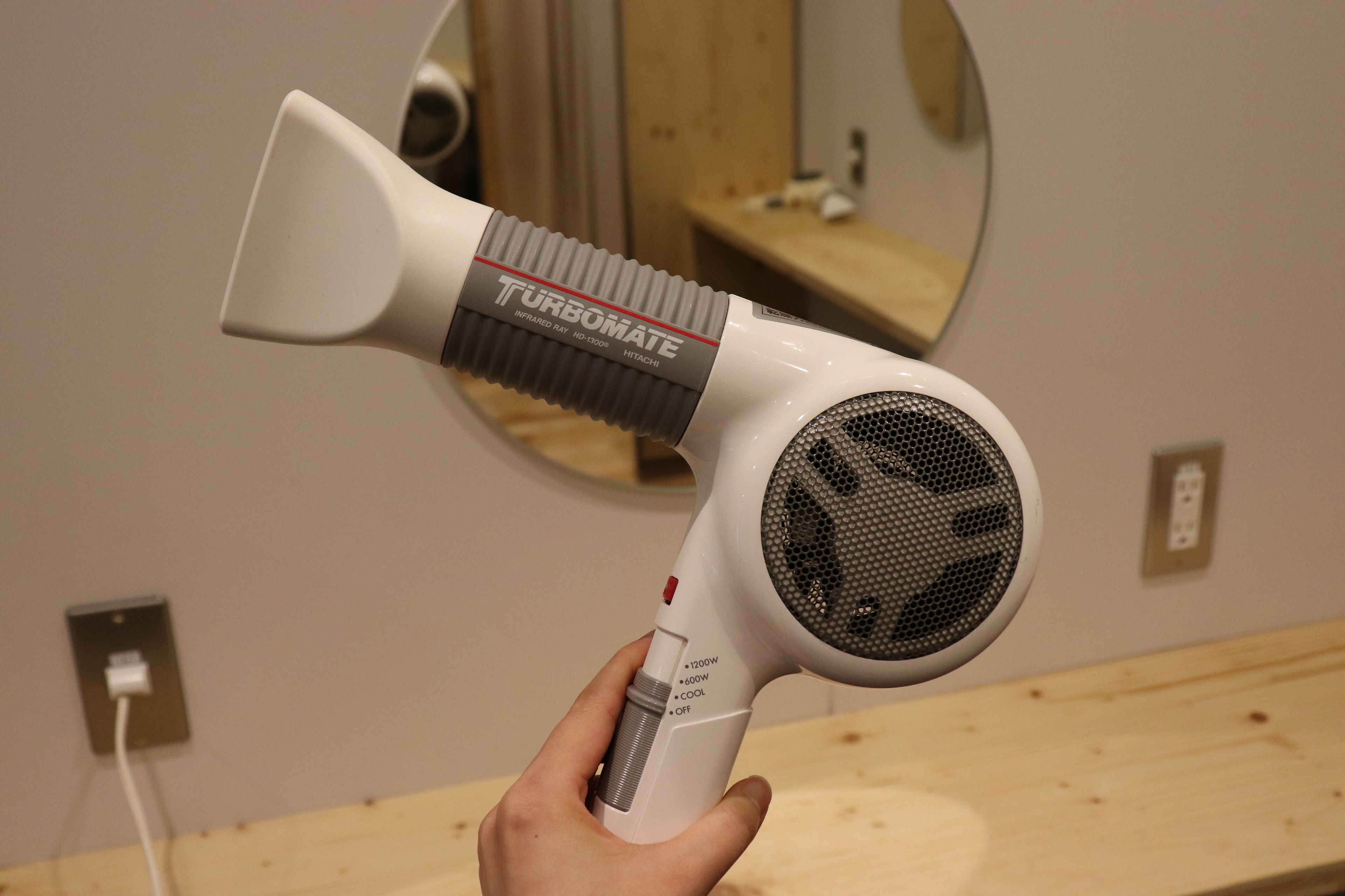 A hand holding a white hair dryer with a "Turbomate" label, a power switch, and a control knob.