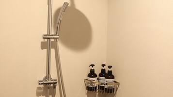 A shower with a handheld showerhead and a wall-mounted faucet. There are three bottles of shampoo on a shelf below.
