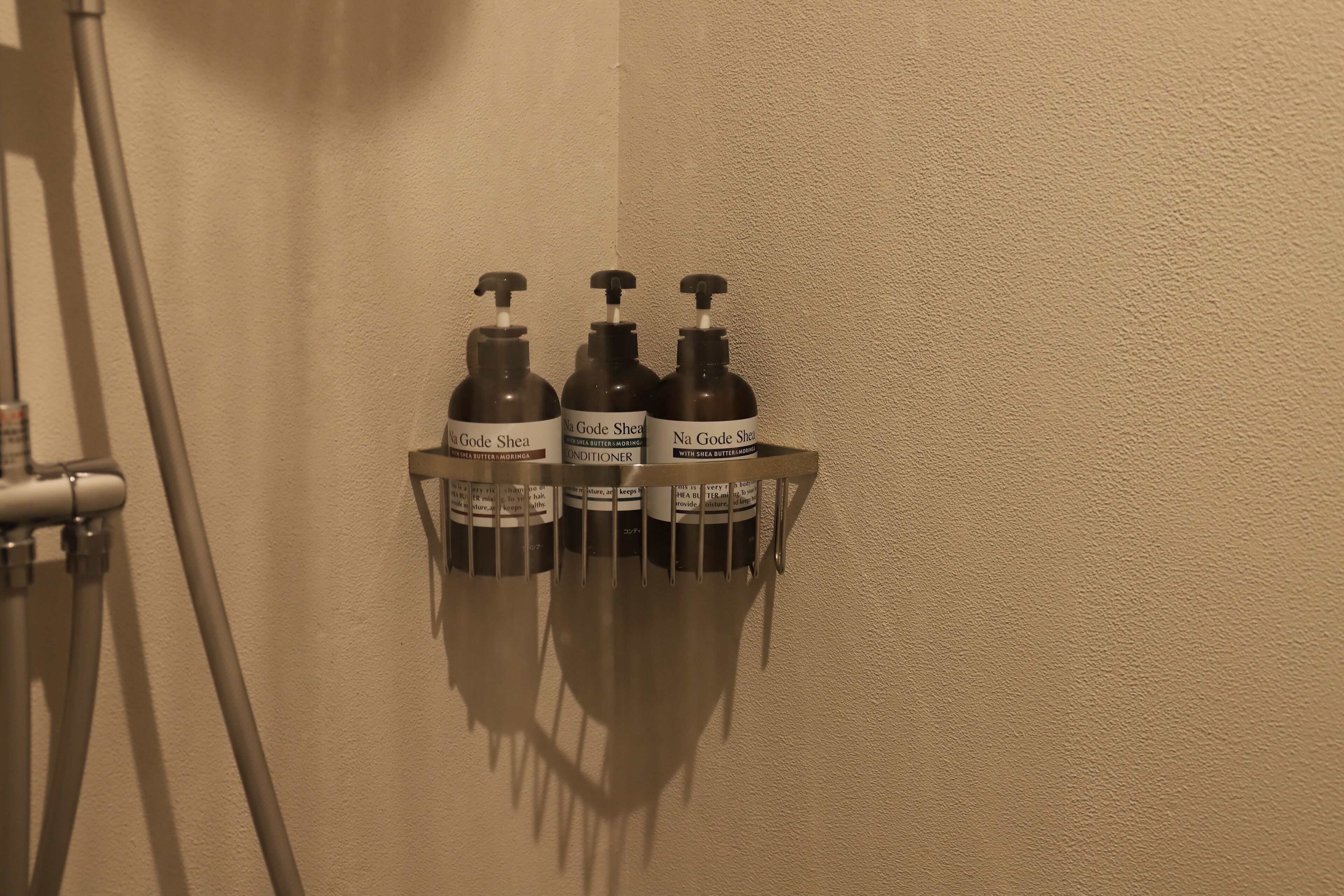 Trois bouteilles d’après-shampoing Na Gode Shea, rangées sur un support mural.