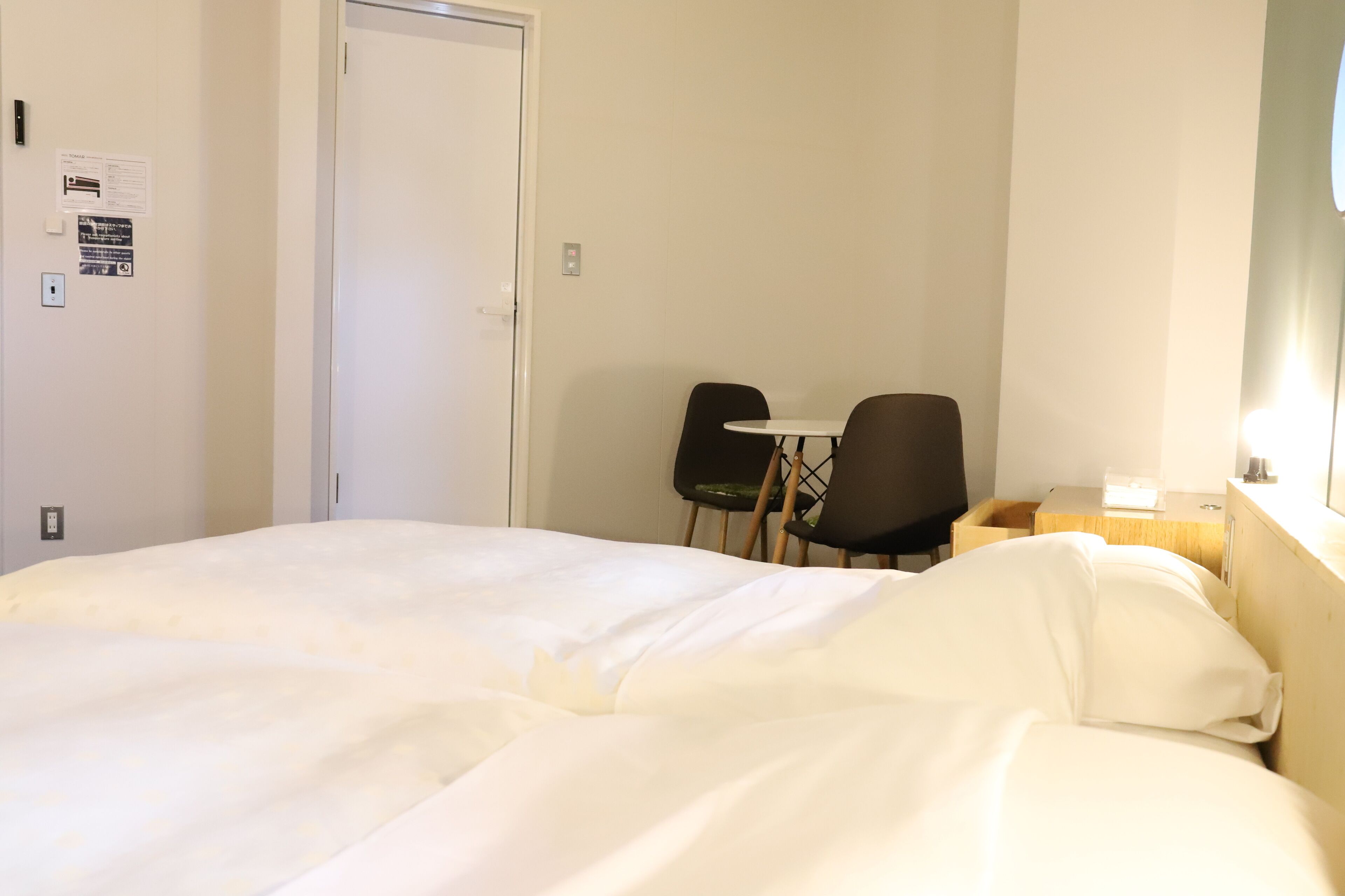 A hotel room with a bed, a desk, two chairs, and a door.