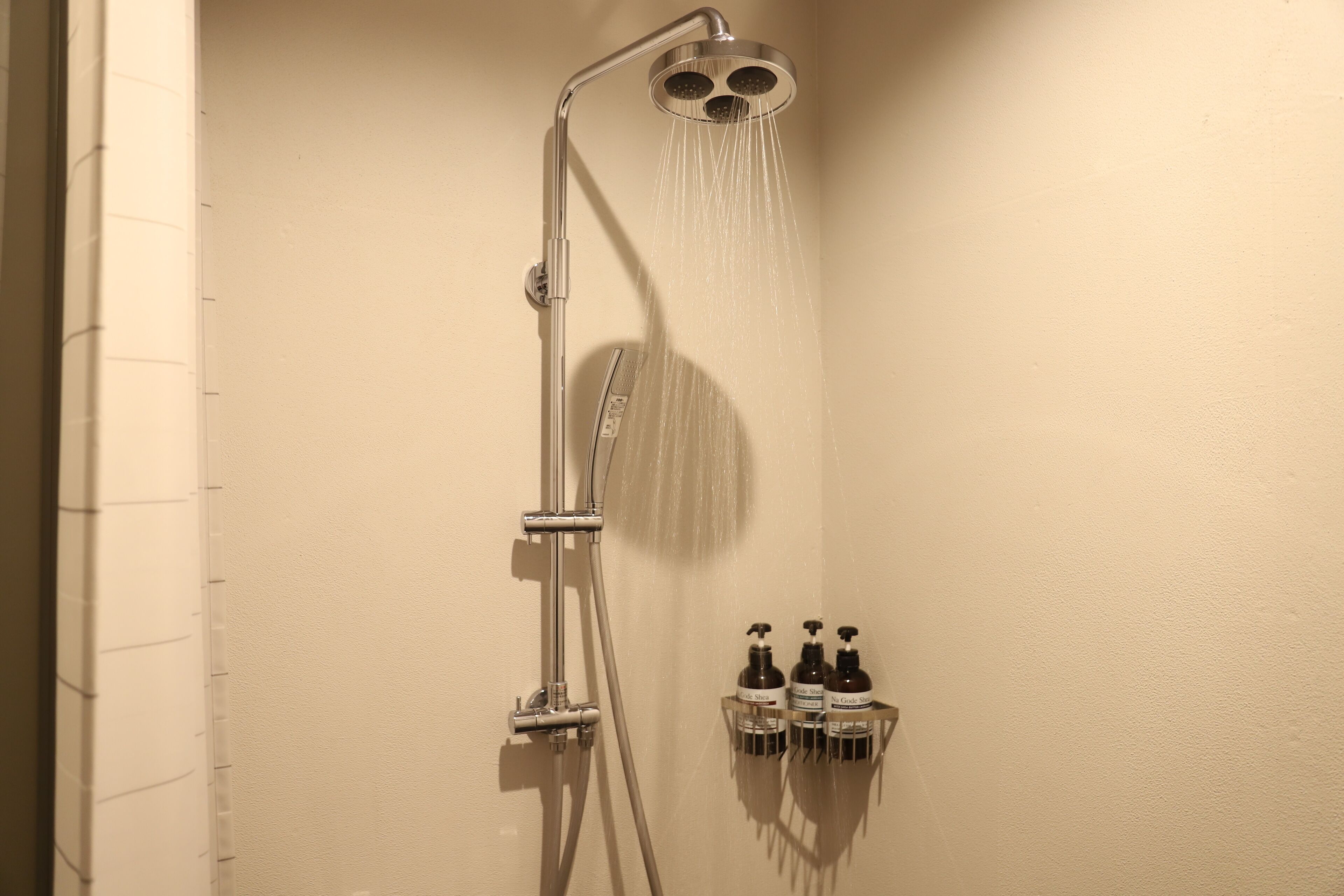 A shower with a handheld showerhead and a wall-mounted faucet. There are two bottles of shampoo and conditioner on a shelf below the shower.