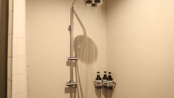 A shower with a handheld showerhead and a wall-mounted faucet. There are two bottles of shampoo and conditioner on a shelf below the shower.