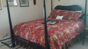 A four-poster bed with a floral bedspread, a bedside table, and a shelf with decorative items.