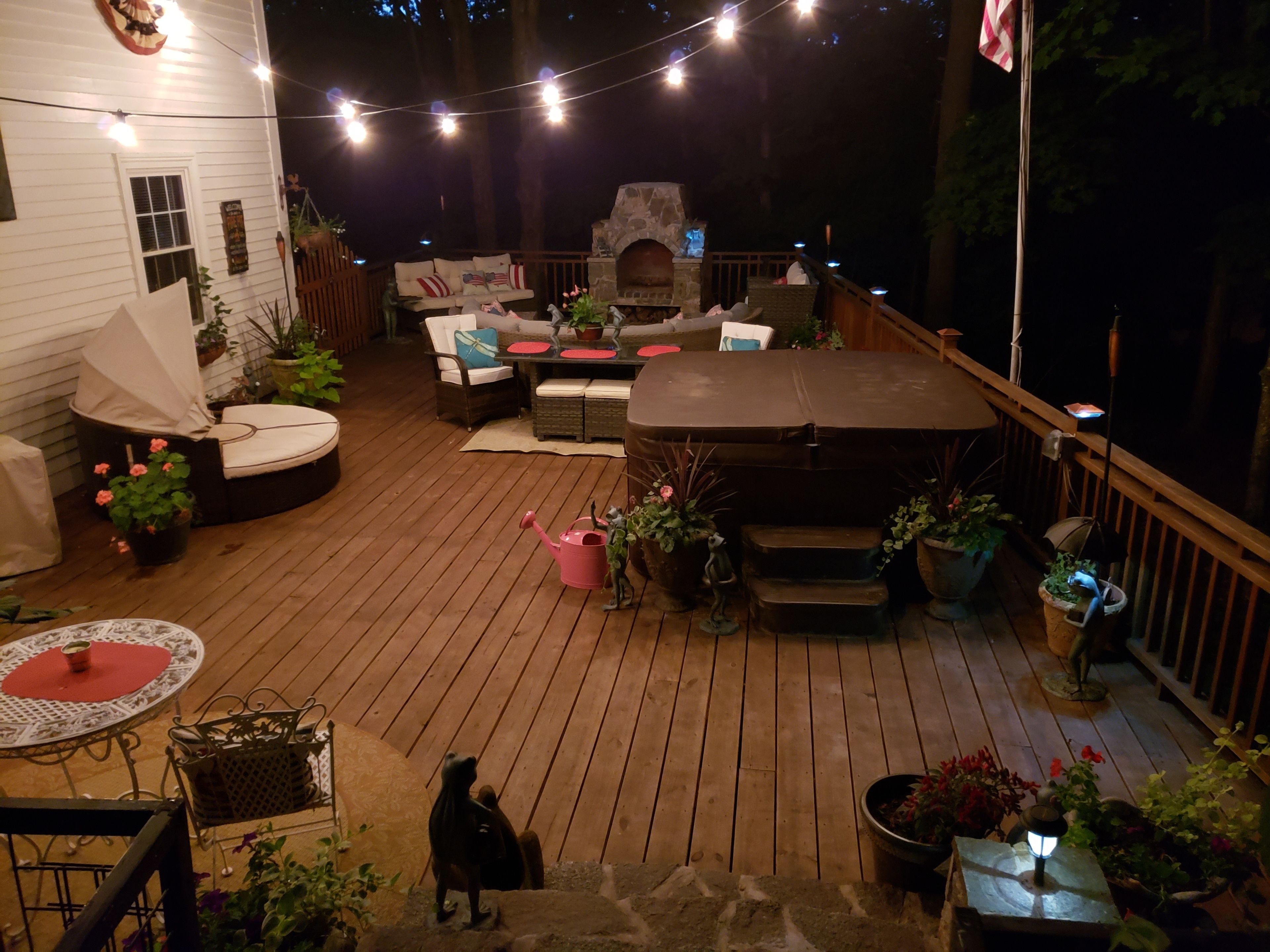 Una terraza de madera con mobiliario exterior, una chimenea de piedra y luces colgantes.