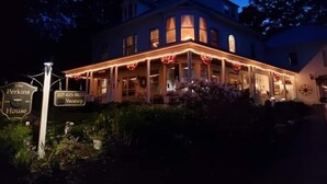 Ein zweistöckiges Gebäude mit einer Veranda, verziert mit roten Bändern und Lichterketten, einem Hinweis auf freie Zimmer und einem Schild mit der Aufschrift "The Perkins House".
