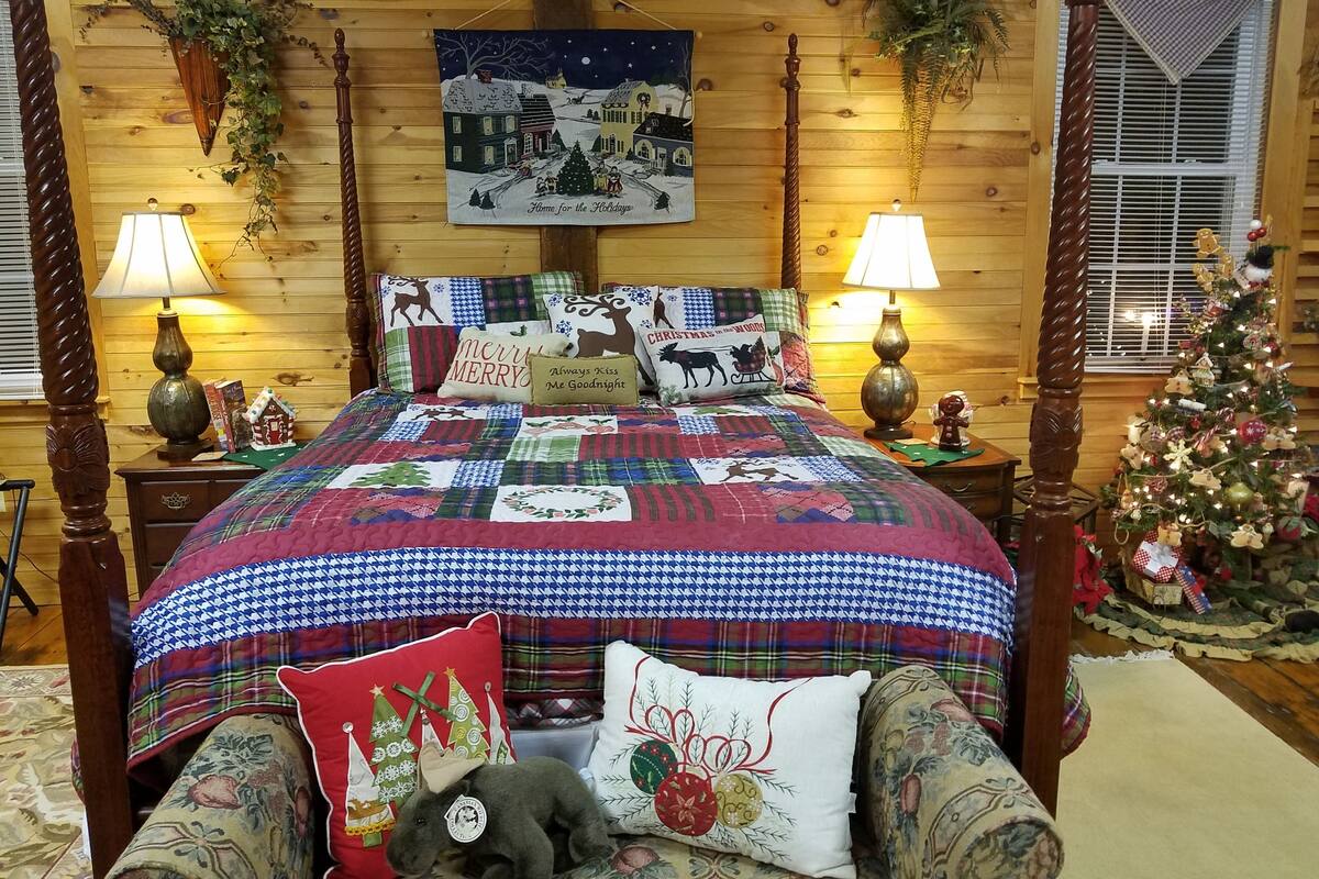 Un dormitorio acogedor con una cama de madera con dosel, un edredón acolchado y almohadas con motivos navideños.