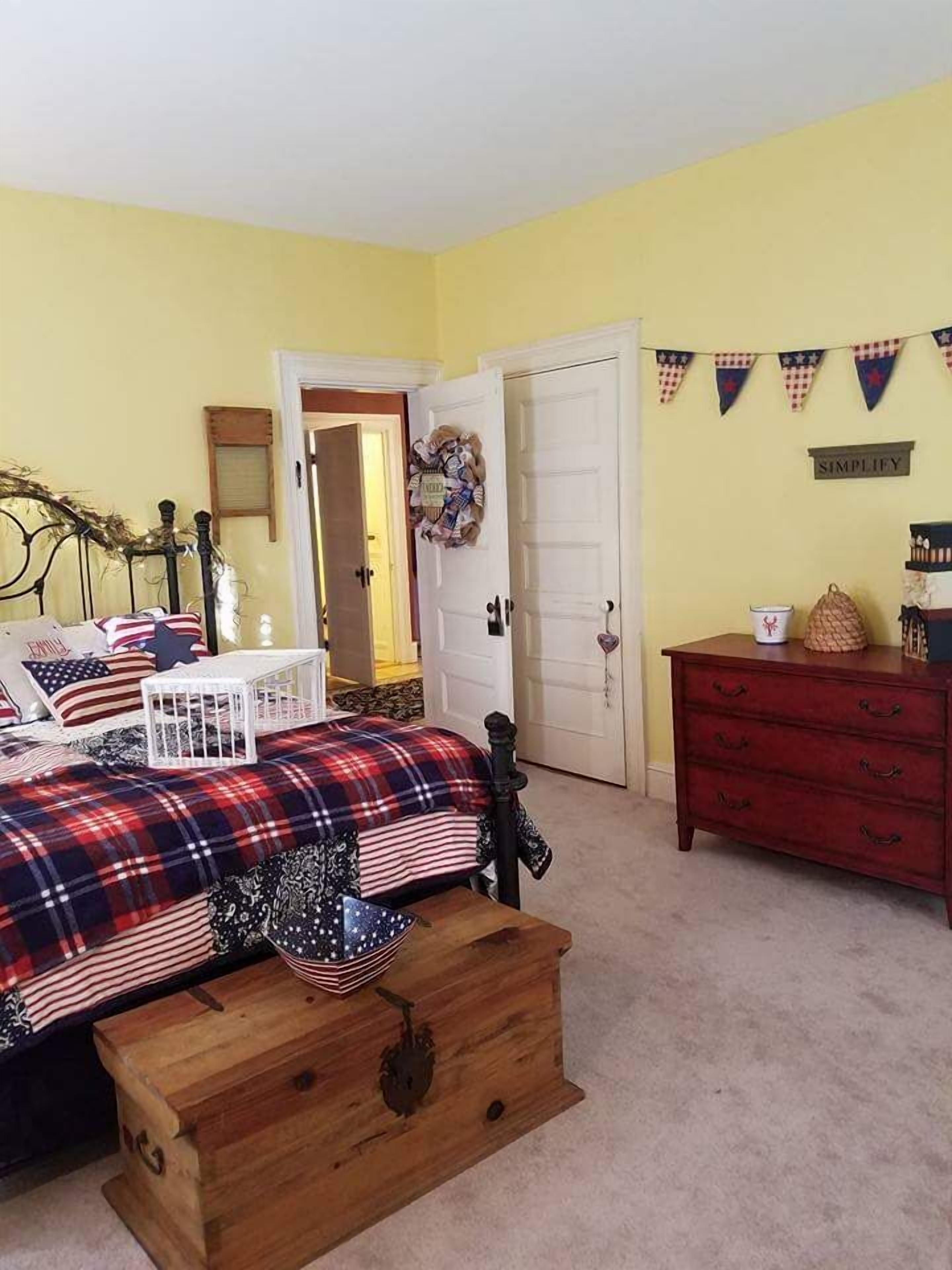 A bedroom with a bed, a dresser, a wooden chest, a door, and a wall with a banner.