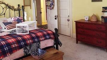 A bedroom with a bed, a dresser, a wooden chest, a door, and a wall with a banner.