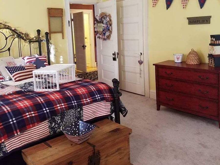A bedroom with a bed, a dresser, a wooden chest, a door, and a wall with a banner.