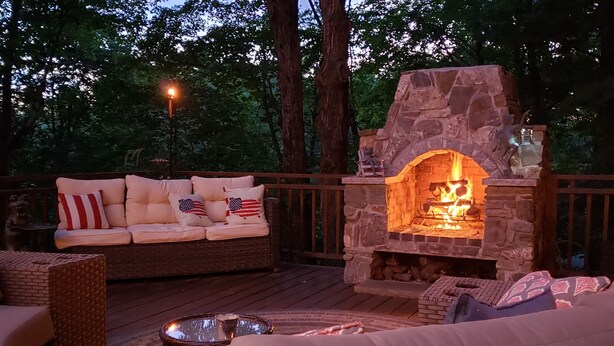 Eine Terrasss mit Kamin aus Stein, einer Couch mit Kissen mit amerikanischer Flagge und einem Korbstuhl.