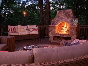 An outdoor deck with a stone fireplace, a sofa with American flag cushions, and a wicker chair. - The Perkins House (Cornish)