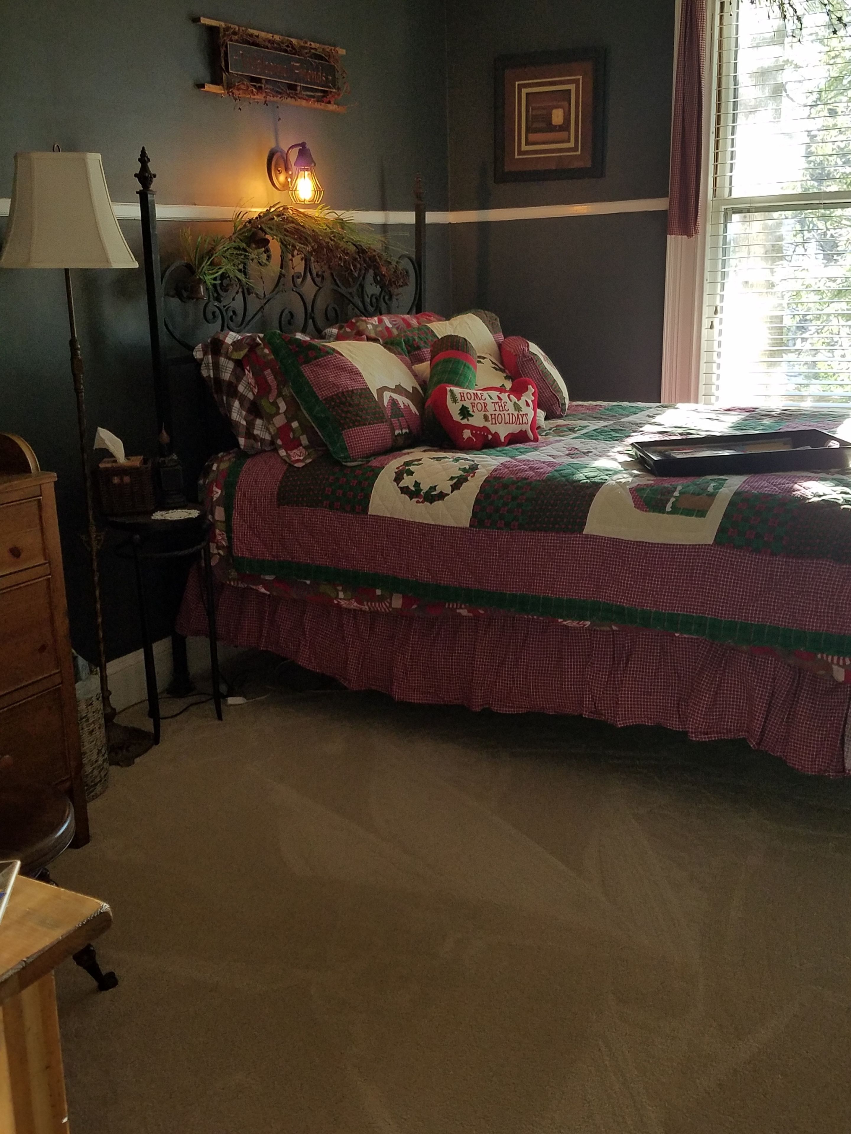 A bedroom with a bed, a nightstand, a lamp, a dresser, and a window with curtains.