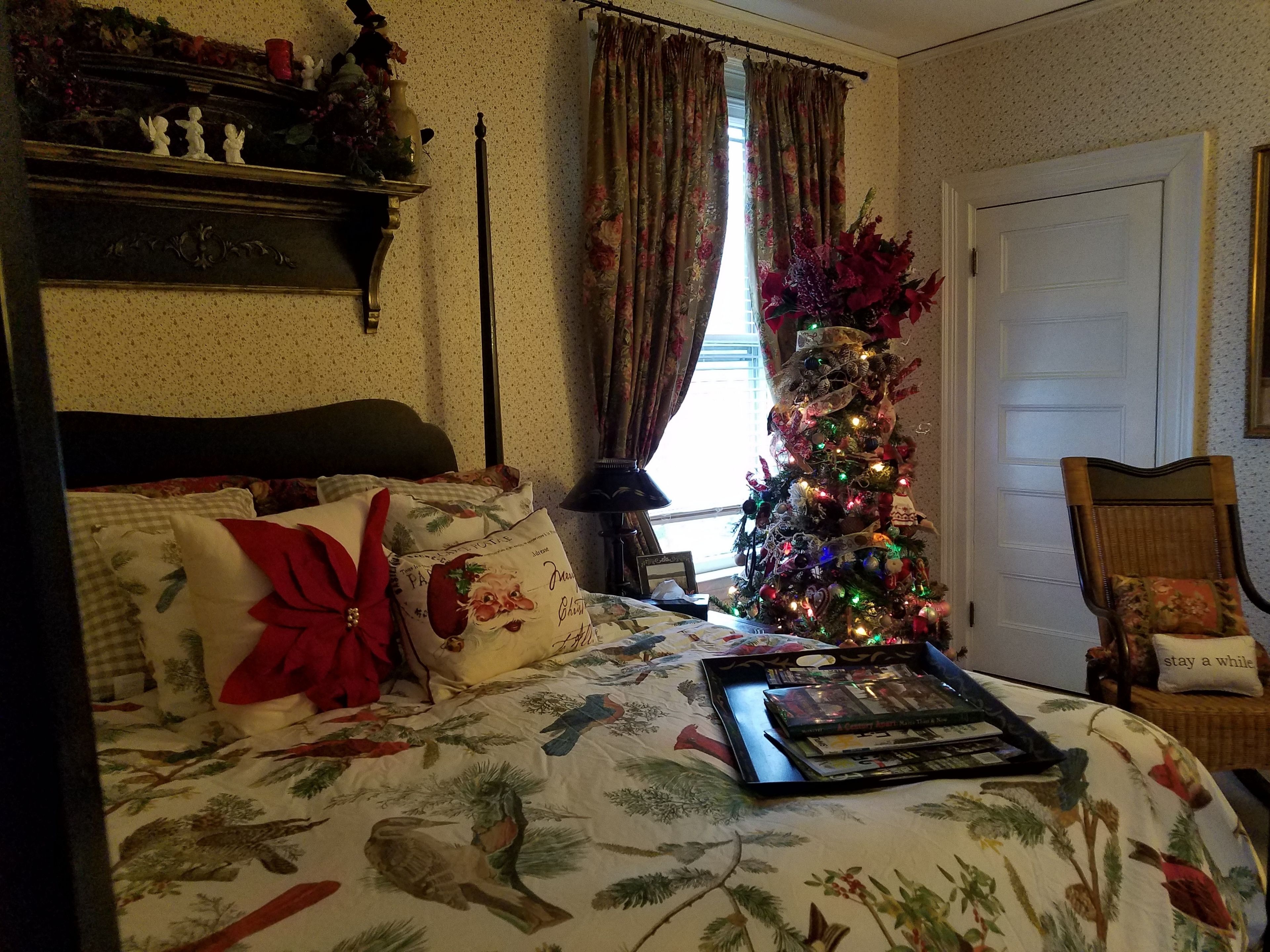A bedroom with a bed, a Christmas tree, a chair, and a door.
