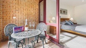 A room with a brick wall, a bed with a grey duvet, a round table with chairs, and a bottle of champagne. - Adelaide Style Accommodation - CLOSE TO CITY - 3Bdrm - In elite North Adelaide (North Adelaide)