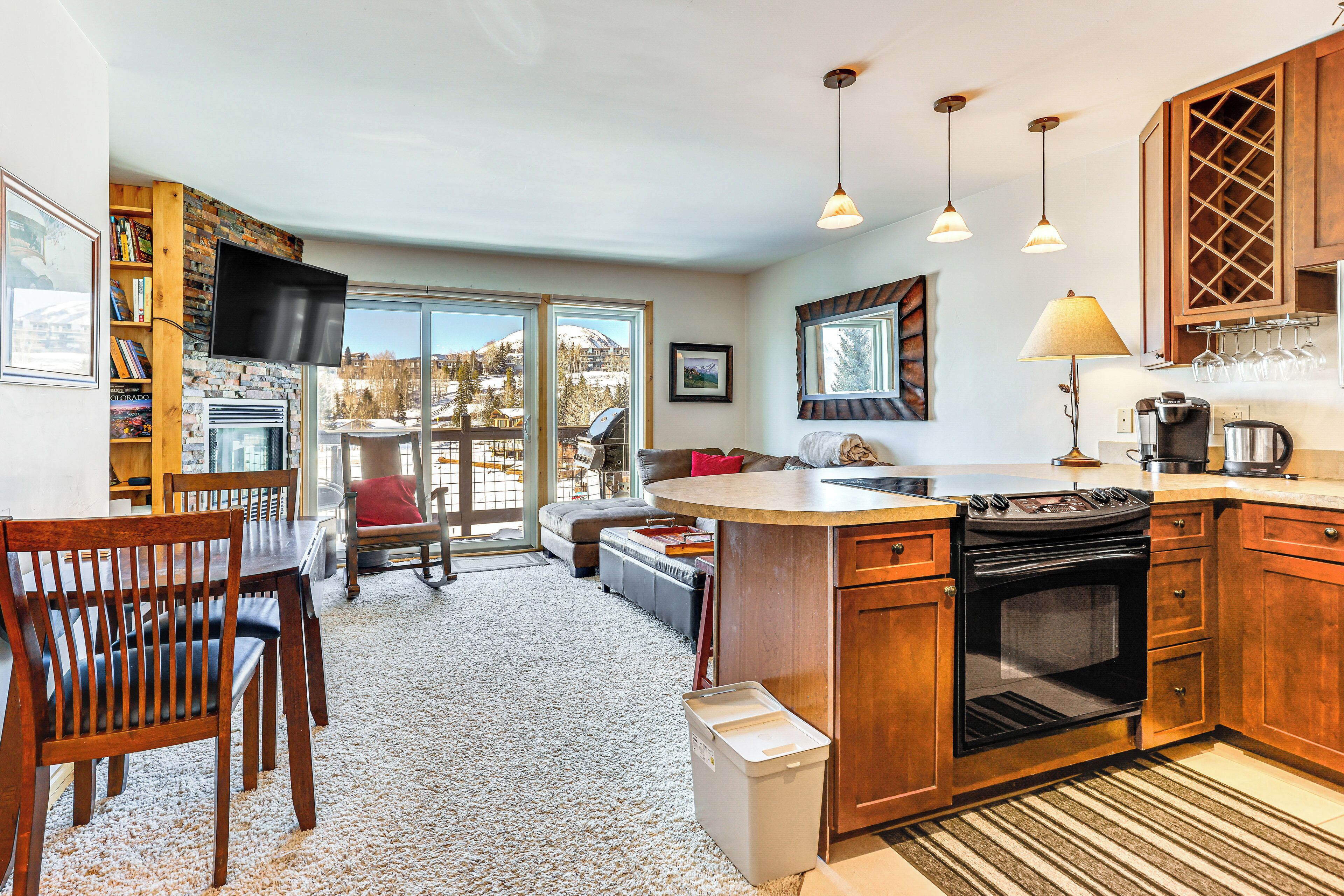 A modern kitchen with a large island, wooden cabinets, a built-in oven, and a dining area with a fireplace.