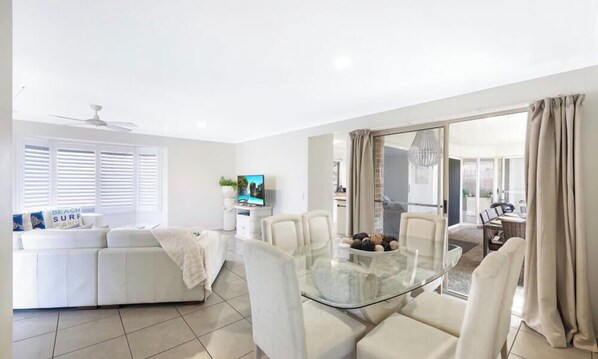 A modern living room with a glass dining table, white sofas, and a TV.