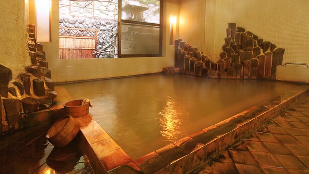 A traditional Japanese onsen with a stone bath, wooden benches, and a view of a garden through a window. - Mogamiya Ryokan (Shiroishi)
