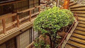 A traditional Japanese building with wooden architecture, a stone wall, and a staircase with a metal railing. - Mogamiya Ryokan (Shiroishi)