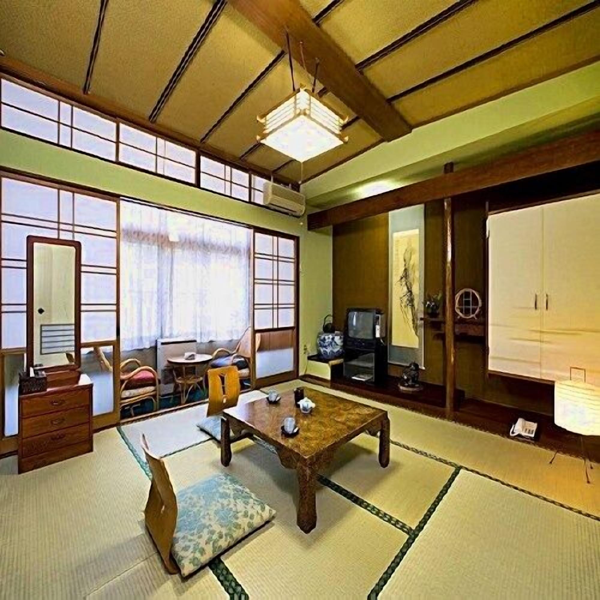 Une pièce de style japonais traditionnel, avec un sol recouvert de tatamis, une table basse, un téléviseur et des portes coulissantes.