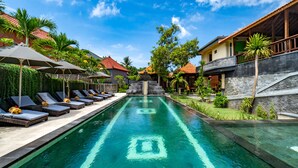 Una piscina con sillas de descanso y sombrillas, rodeada de edificios con tejados rojos y vegetación.