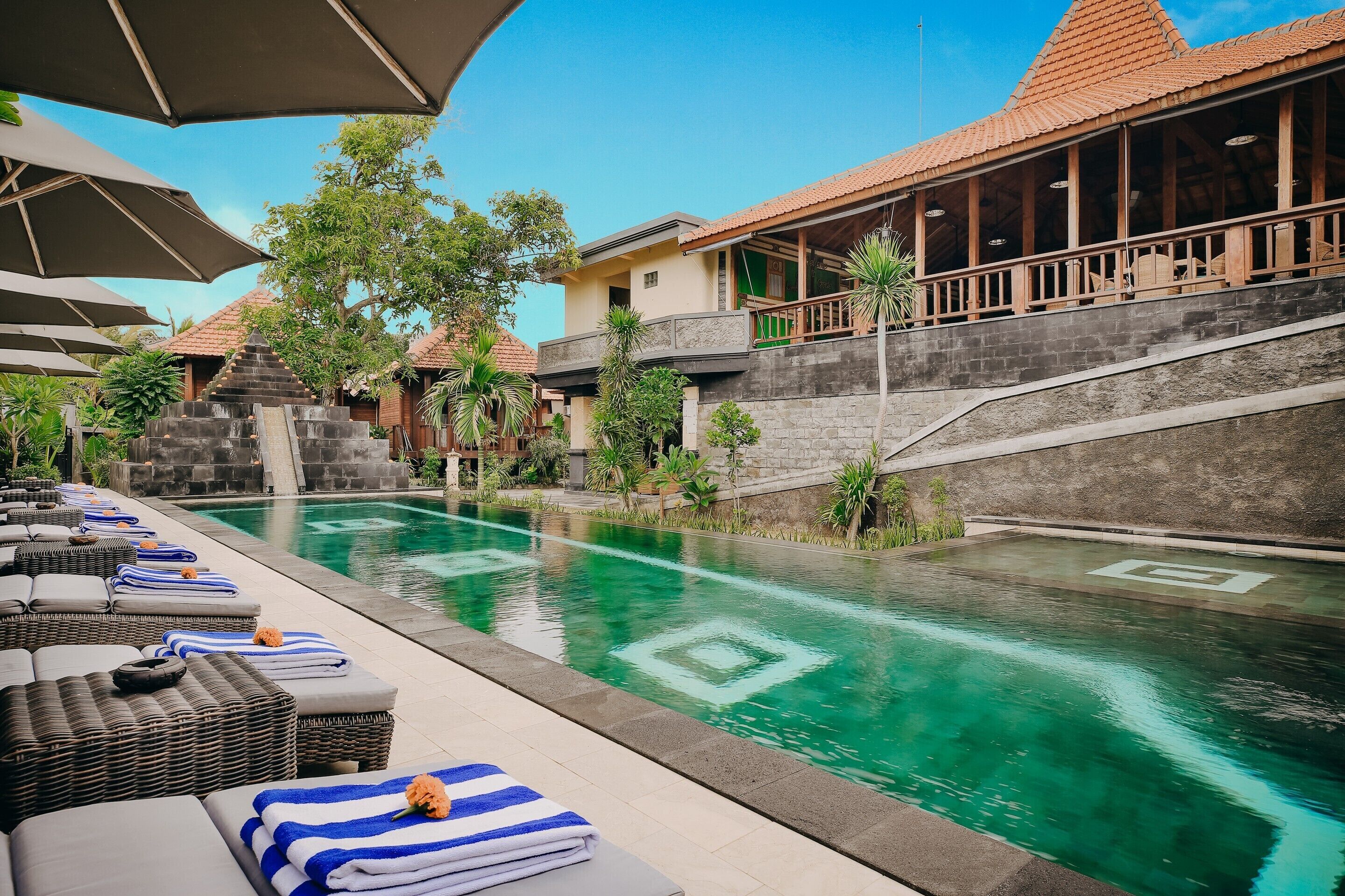 Un espace piscine avec des chaises longues et des parasols, un escalier en pierre et un bâtiment doté d’un toit en tuiles.