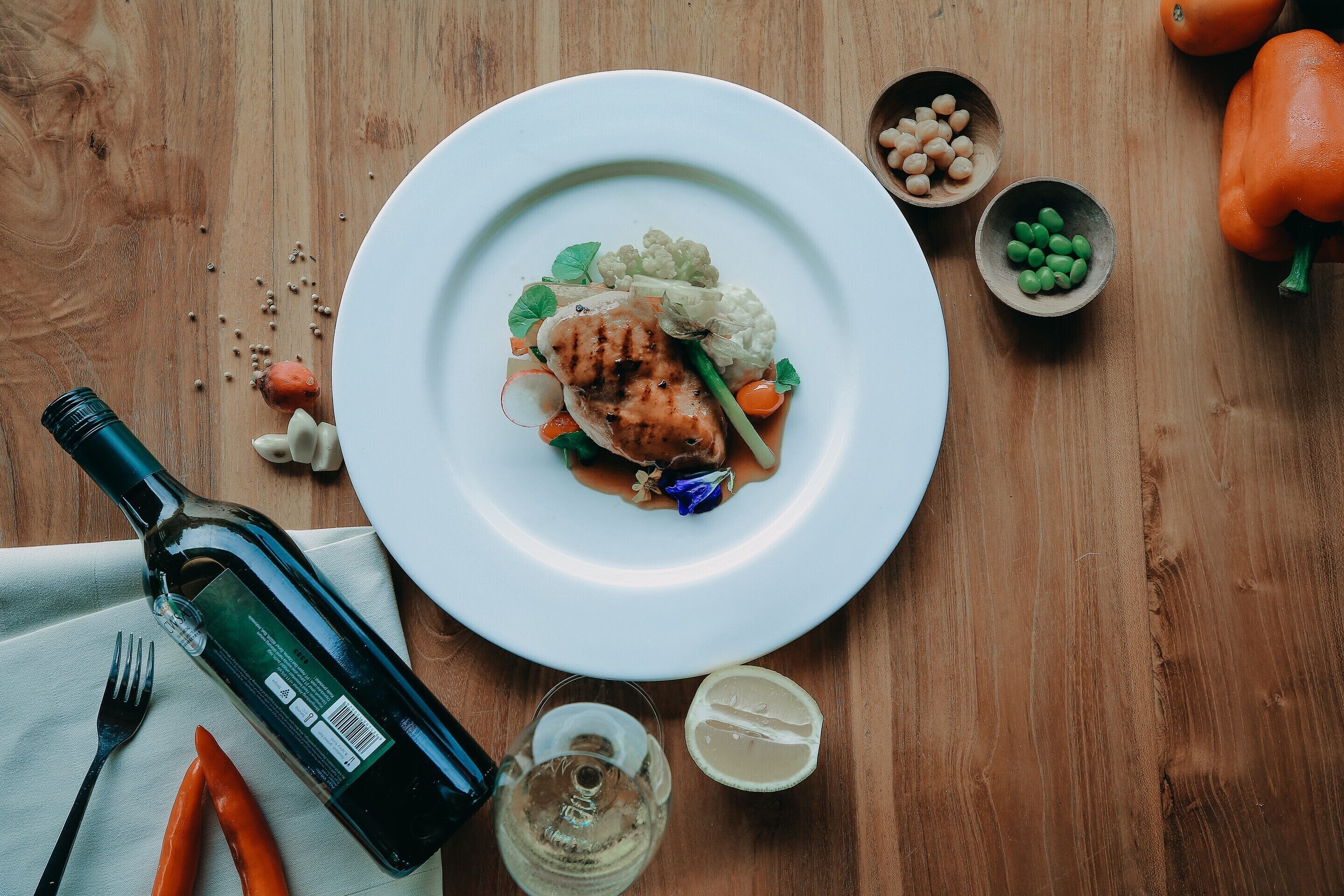 Een bord eten met een fles, een glas en wat groenten op een houten tafel.