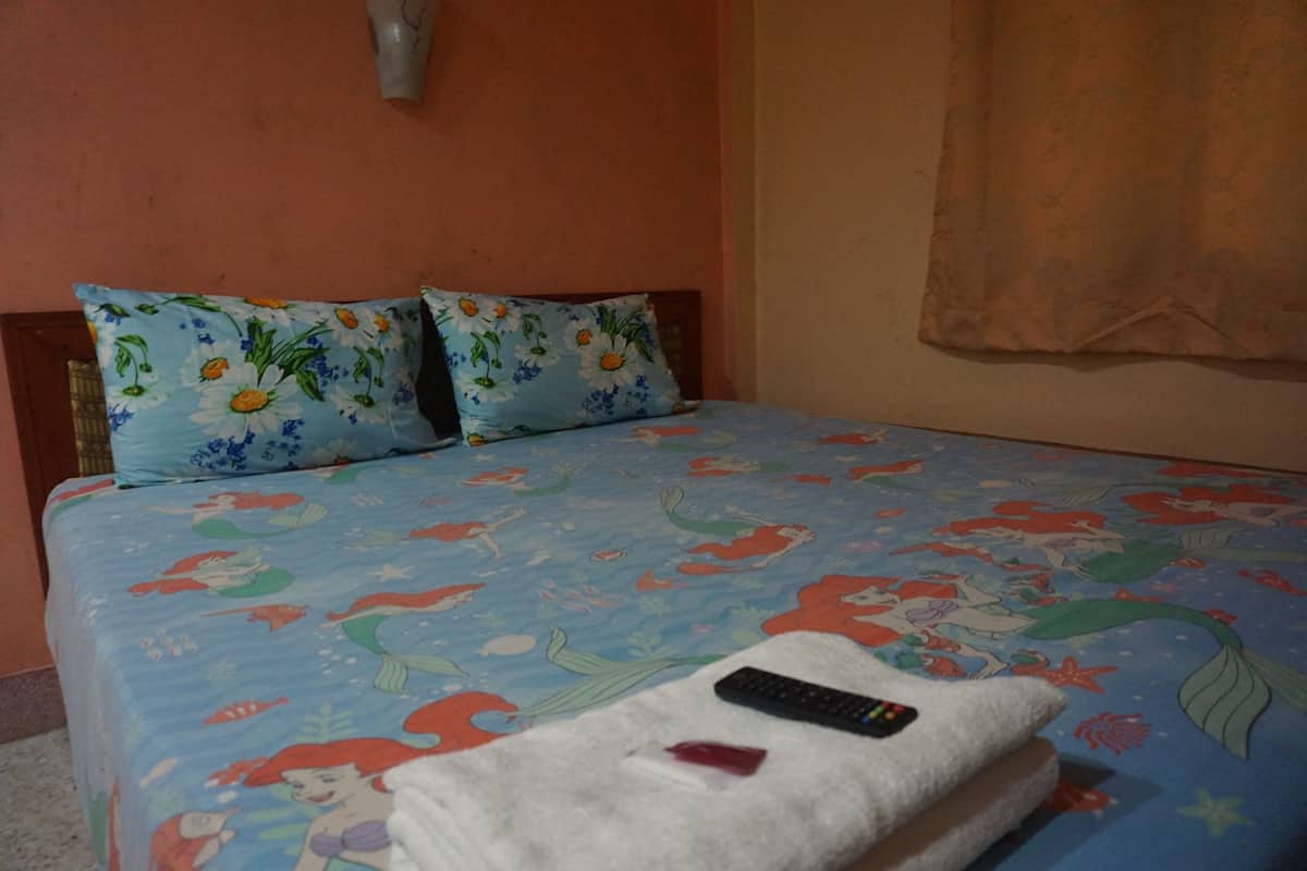 A bed with a mermaid-themed bedspread, a remote control, and a white towel on it.