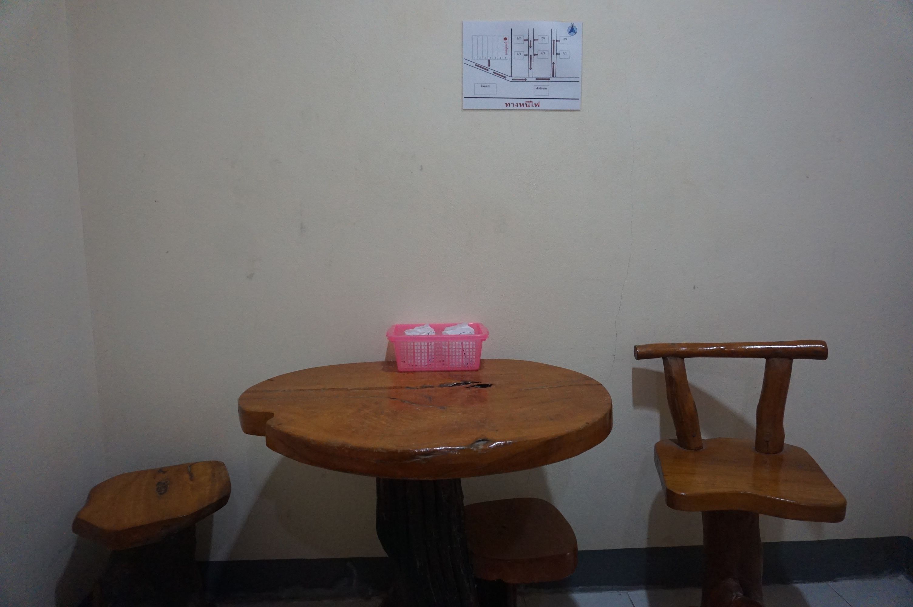 A small wooden table with a pink basket on it, two wooden chairs, and a wall-mounted sign.