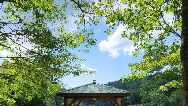 A gazebo with a bench, a wooden dock, and a gravel path leading to a lake.