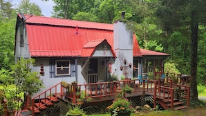A rustic cabin with a red roof, a wooden deck, and a staircase leading to the entrance.