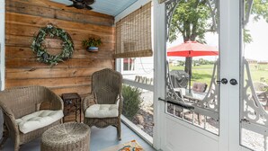 A porch with wicker furniture, a ceiling fan, a wooden wall, a door with a glass panel, and a red umbrella outside. - Historical Property, Mountain View’s quiet country life. (Stanley)
