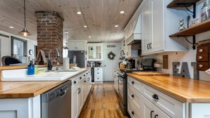 A kitchen with wooden countertops, white cabinets, and a brick wall. - Historical Property, Mountain View’s quiet country life. (Stanley)