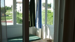 A room with a bed, a small table, and a view of greenery and buildings outside. - Apartment Studio A2_Croatia, Istria, Medulin (Medulin)