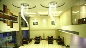 A lobby with a marble floor, black sofas, a chandelier, and framed artwork on the walls. - Castle Inn (Khandwa)