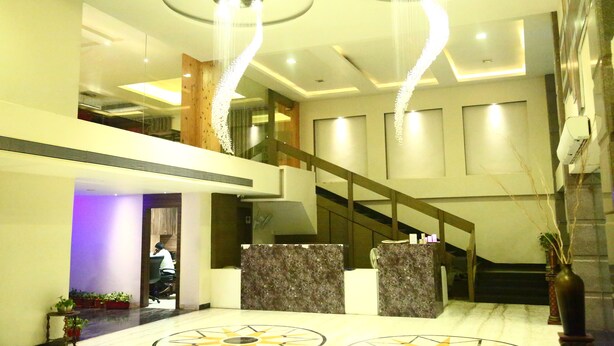 A hotel lobby with a marble reception desk, a staircase, and a modern chandelier. - Castle Inn (Khandwa)