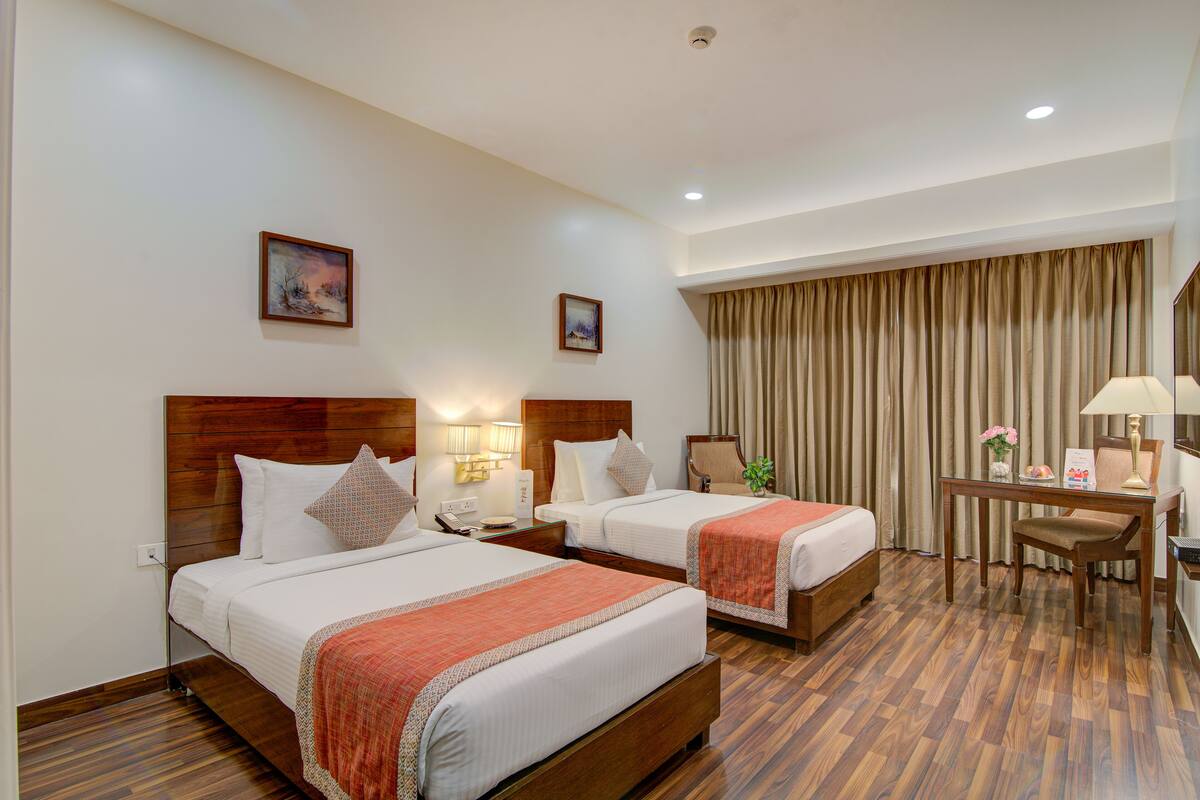 A hotel room with two beds, a desk, a chair, and a curtain.