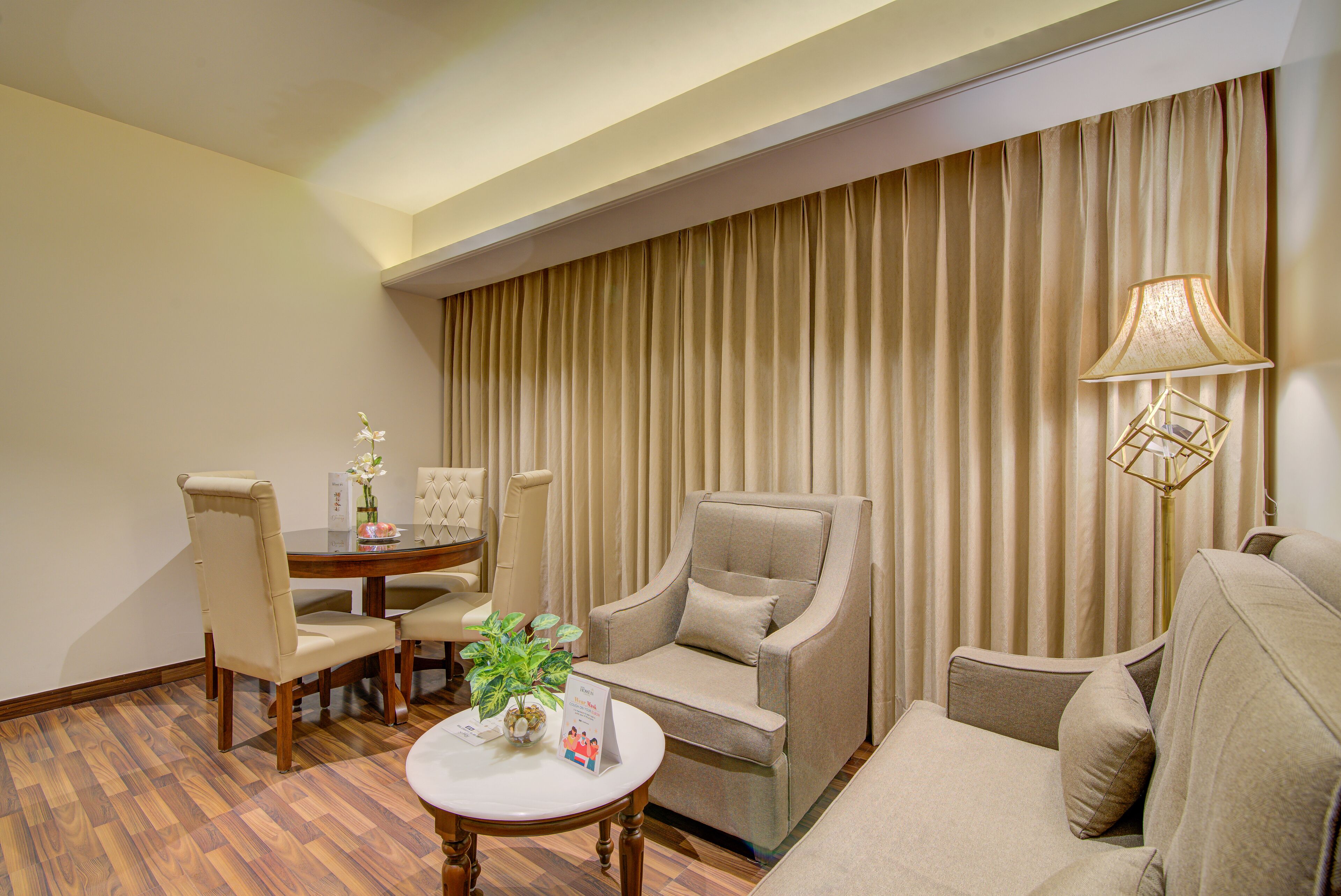 A hotel room with a dining area, a sofa, a chair, a lamp, and a potted plant.