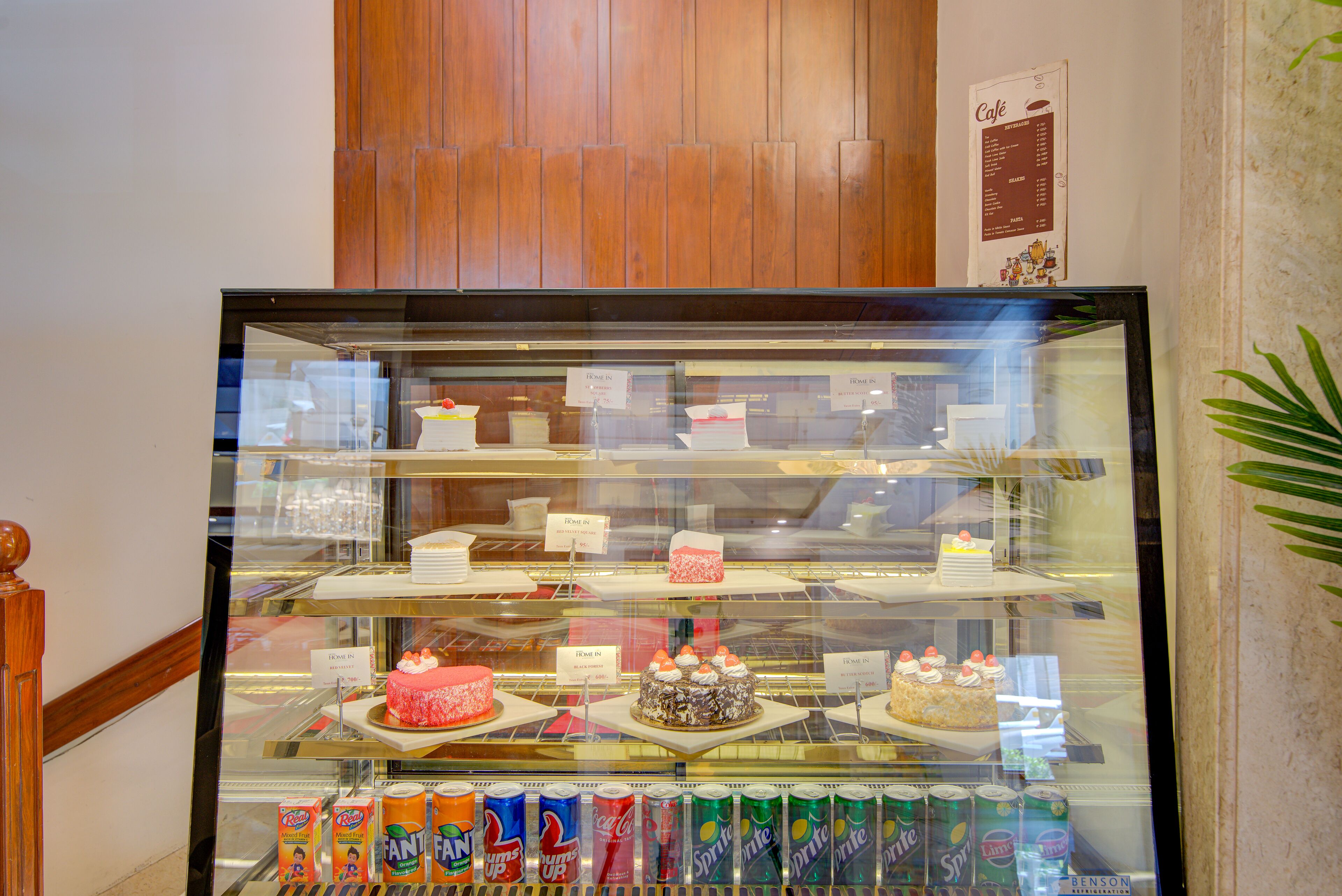 A bakery display case with various cakes and a selection of soda cans.