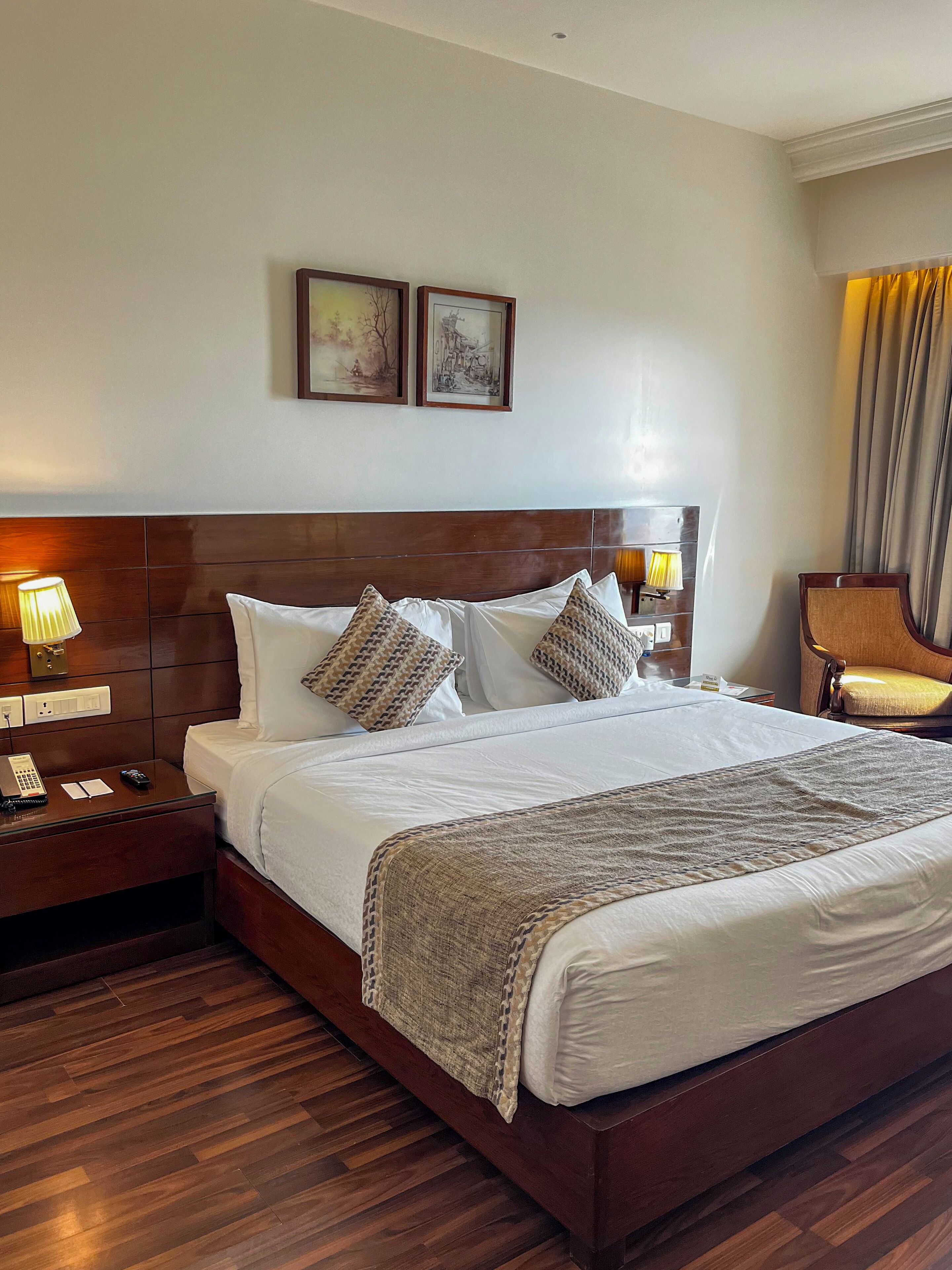 A hotel room with a large bed, wooden headboard, two bedside lamps, a nightstand, and a chair.