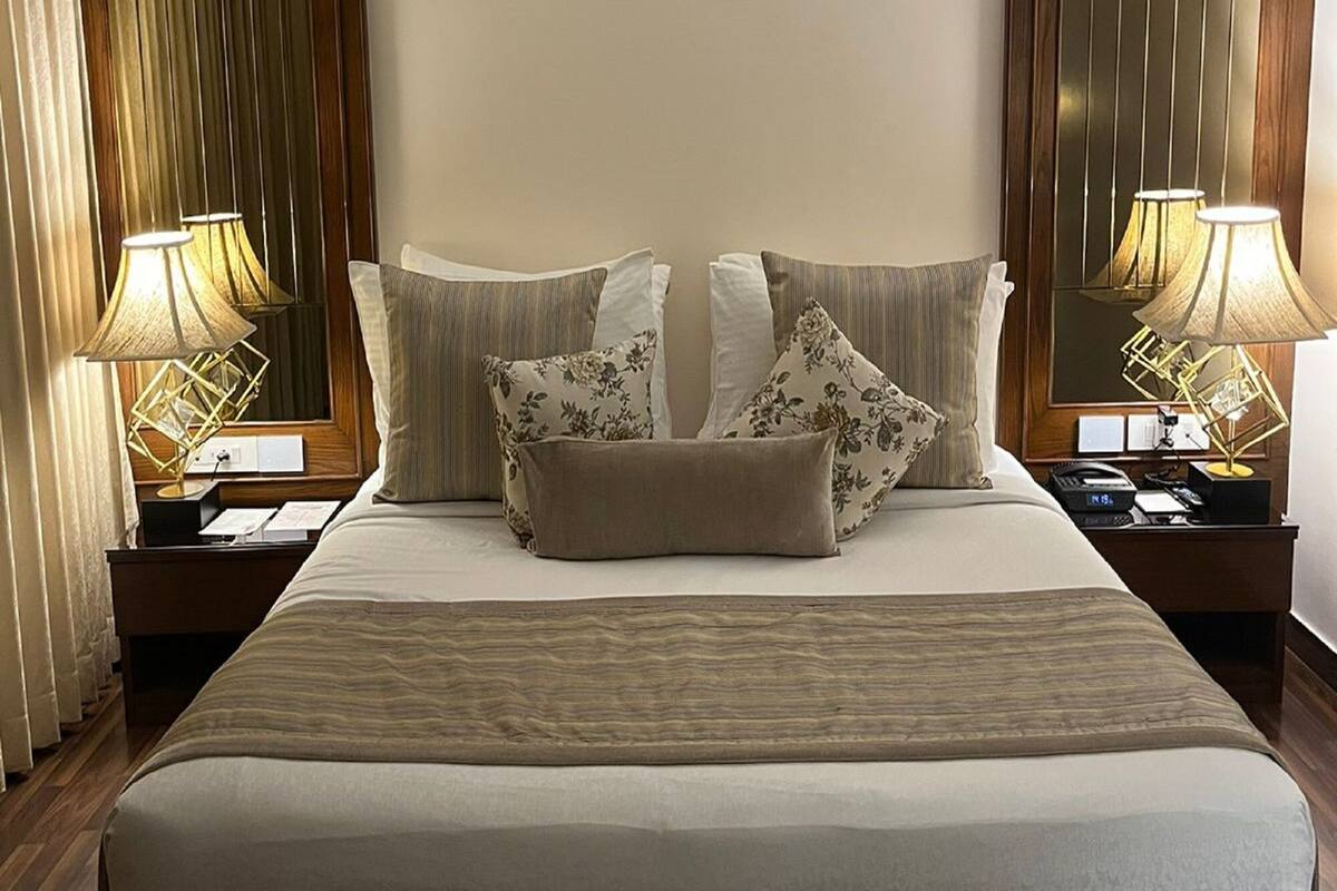 A large bed with a wooden headboard, two bedside lamps, and a mirror on the wall.