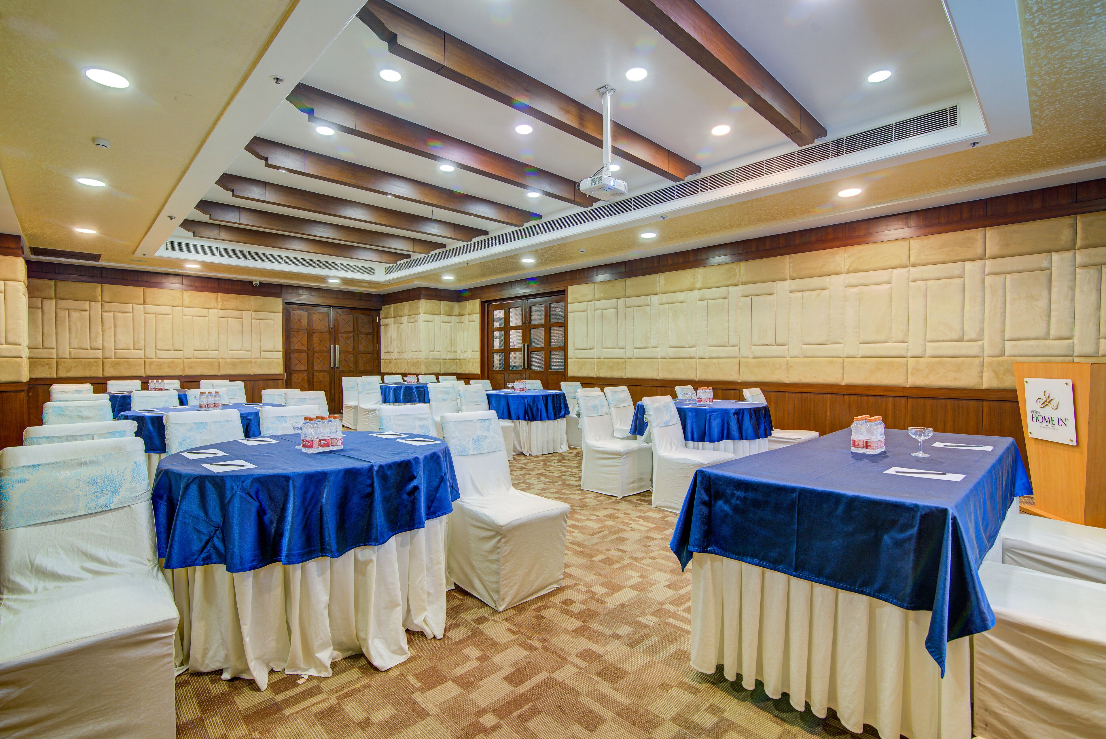 Une salle de conférence équipée de tables et de chaises, d’un ventilateur de plafond et d’une enseigne indiquant le nom de la salle.