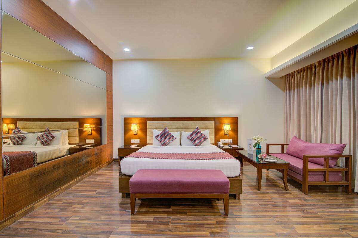 A modern hotel room with a large bed, bedside tables, a sofa, and a mirror.