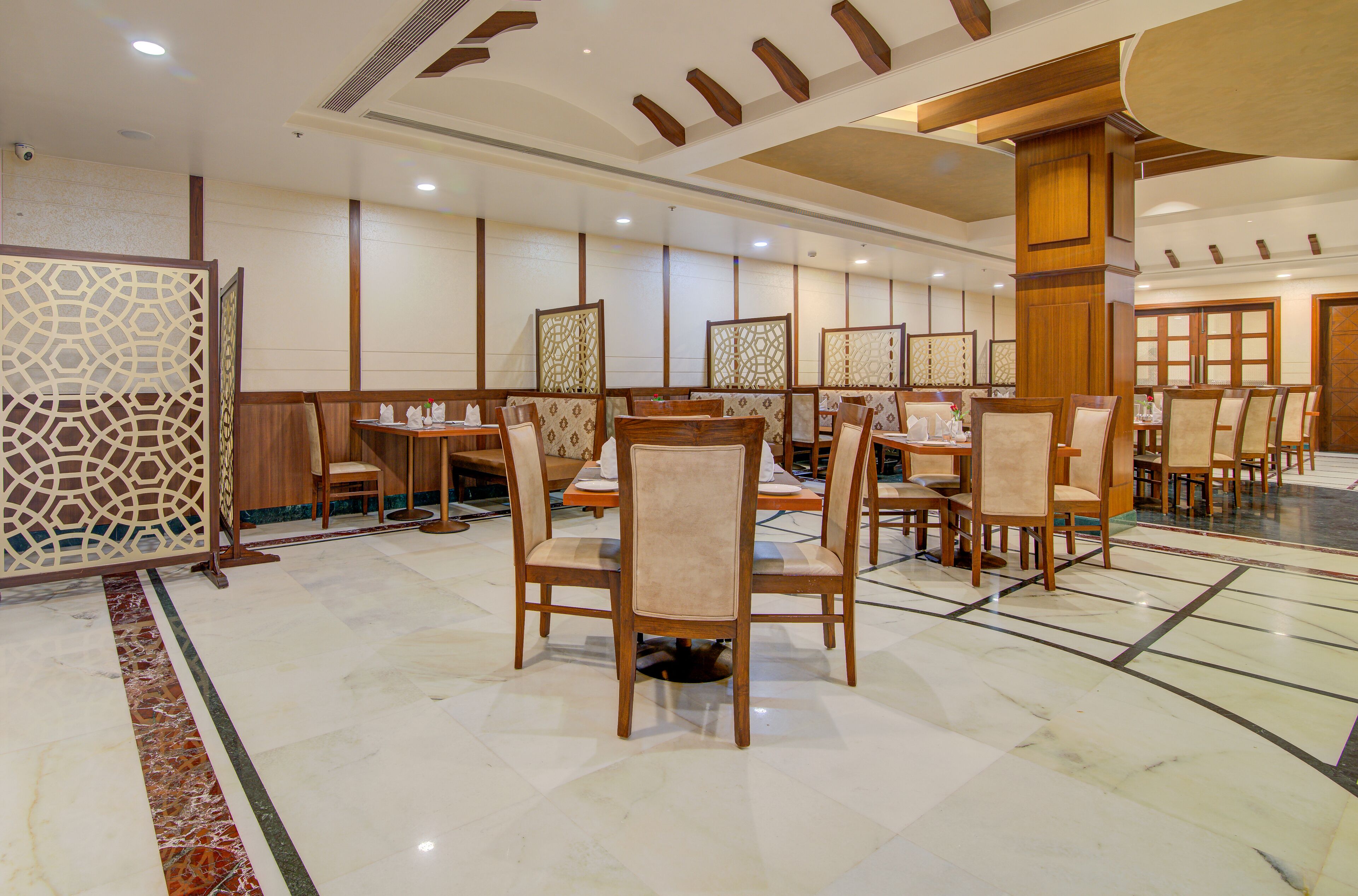 A spacious dining area with multiple tables and chairs, wooden paneling on the walls, and a marble floor.