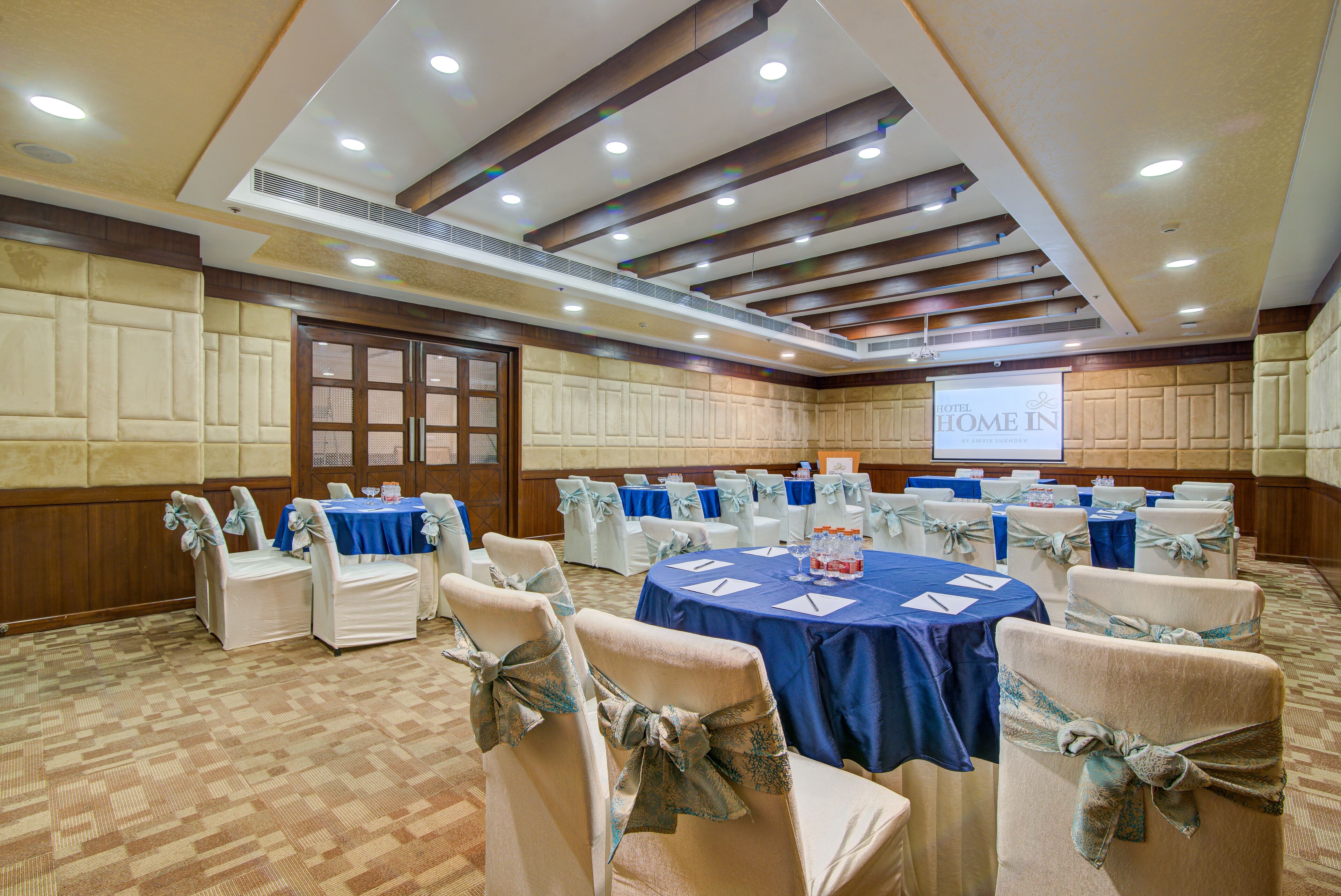 Un salón de conferencias con mesas redondas, sillas blancas y manteles azules.