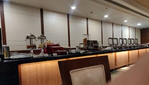 A buffet setup with multiple food dispensers, a coffee machine, and a red cash register.